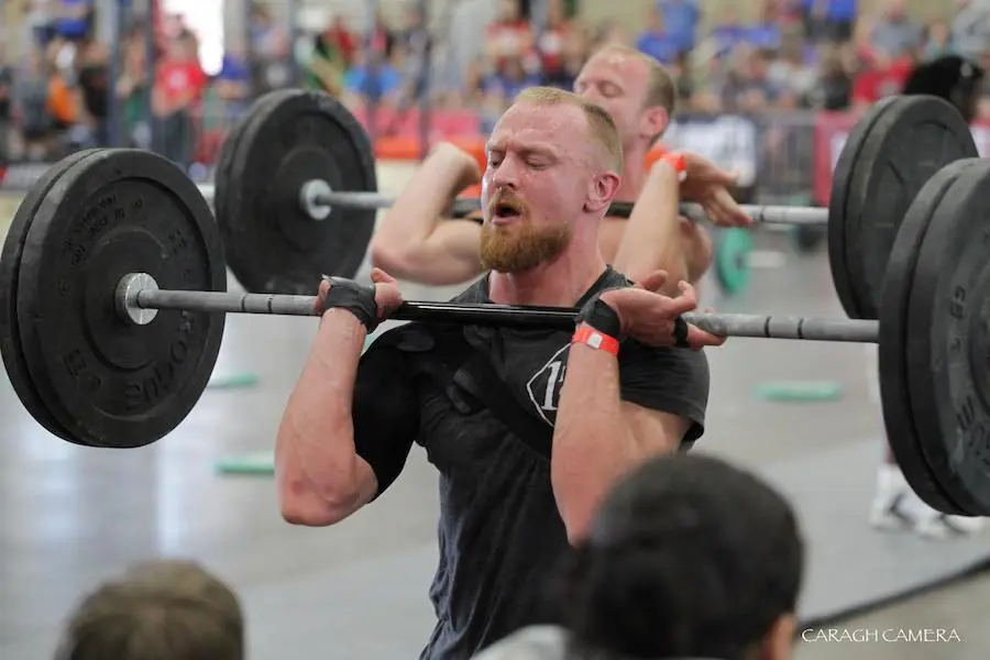 front squat A man focuses on lifting a weighted barbell during a competition, with spectators in the background. Sports Medicine Northwest - West Seattle Chiropractic Clinic