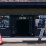 The entrance of a CrossFit gym at 2920 showcases two sandwich boards on the sidewalk, photos of gym equipment on the windows, and offers guidance from a sports chiropractor for effective lower back exercises as part of their prehab program. Sports Medicine Northwest - West Seattle Chiropractic Clinic