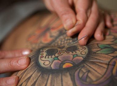 Close-up of a tattoo artist's hand skillfully using a needle to ink a colorful design on a person's skin, much like the precision required in sports acupuncture. Sports Medicine Northwest - West Seattle Chiropractic Clinic