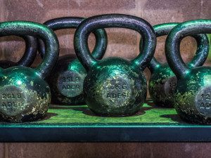 A row of worn green kettlebells on a shelf, labeled with weights in kilograms and pounds. Sports Medicine Northwest - West Seattle Chiropractic Clinic