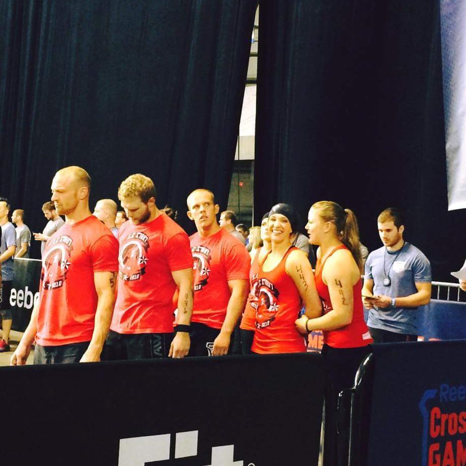 At the West Regionals, a group of people in red shirts stands lined up in an indoor arena. Some have numbers on their arms, suggesting a challenging day ahead. Sports Medicine Northwest - West Seattle Chiropractic Clinic