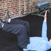 Person in a blue hoodie focuses on midline stability while performing a dead bug exercise on a gym mat, with legs bent and arms extended, next to a brick wall. Sports Medicine Northwest - West Seattle Chiropractic Clinic