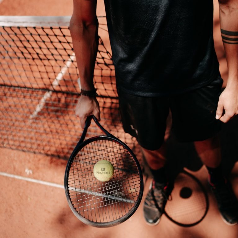 person in black shorts holding green tennis racket