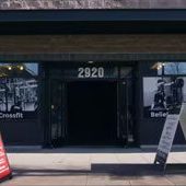 The entrance of a CrossFit gym at 2920 showcases two sandwich boards on the sidewalk, photos of gym equipment on the windows, and offers guidance from a sports chiropractor for effective lower back exercises as part of their prehab program. Sports Medicine Northwest - West Seattle Chiropractic Clinic