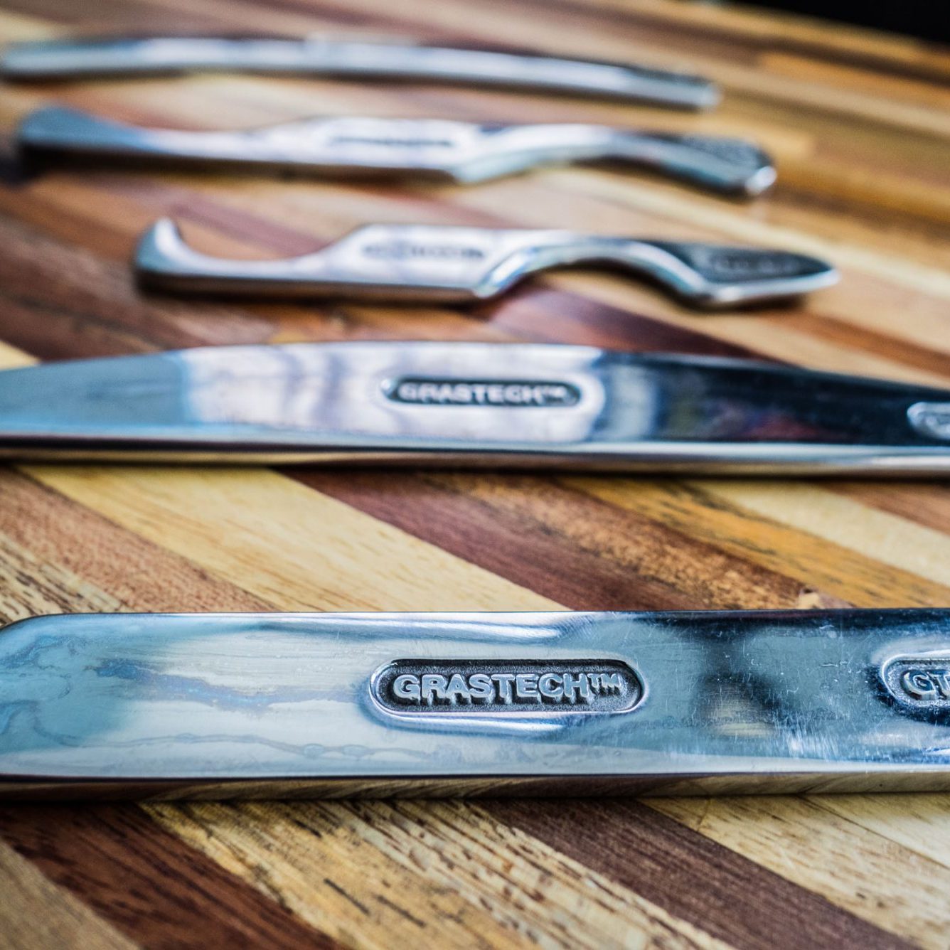 A set of five polished metal Graston tools of varying shapes and sizes laid out on a wooden surface. Sports Medicine Northwest - West Seattle Chiropractic Clinic